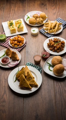 Indian Tea time snacks  in group includes Veg Samosa, Kachori/kachaudi, aloo bonda, khaman dhokla, bread, onion,chilli and moong pakora/pakoda/bhaji/bhajji/Bhajiya/bajji with sauces, selective focus