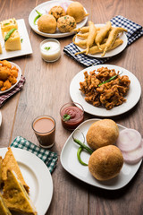 Indian Tea time snacks  in group includes Veg Samosa, Kachori/kachaudi, aloo bonda, khaman dhokla, bread, onion,chilli and moong pakora/pakoda/bhaji/bhajji/Bhajiya/bajji with sauces, selective focus