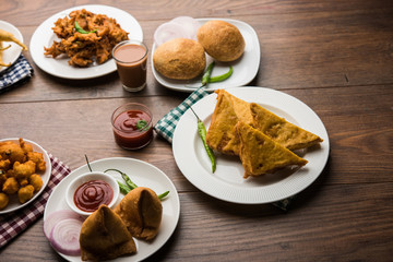 Indian Tea time snacks  in group includes Veg Samosa, Kachori/kachaudi, aloo bonda, khaman dhokla, bread, onion,chilli and moong pakora/pakoda/bhaji/bhajji/Bhajiya/bajji with sauces, selective focus