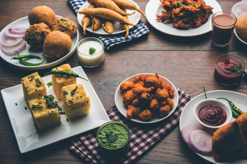 Indian Tea time snacks  in group includes Veg Samosa, Kachori/kachaudi, aloo bonda, khaman dhokla, bread, onion,chilli and moong pakora/pakoda/bhaji/bhajji/Bhajiya/bajji with sauces, selective focus