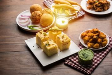 Indian Tea time snacks  in group includes Veg Samosa, Kachori/kachaudi, aloo bonda, khaman dhokla, bread, onion,chilli and moong pakora/pakoda/bhaji/bhajji/Bhajiya/bajji with sauces, selective focus