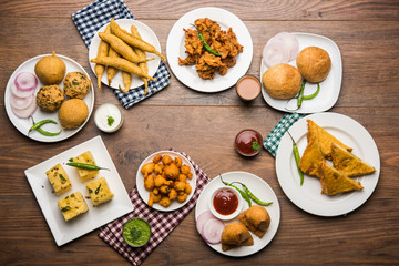 Indian Tea time snacks  in group includes Veg Samosa, Kachori/kachaudi, aloo bonda, khaman dhokla, bread, onion,chilli and moong pakora/pakoda/bhaji/bhajji/Bhajiya/bajji with sauces, selective focus