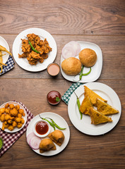 Indian Tea time snacks  in group includes Veg Samosa, Kachori/kachaudi, aloo bonda, khaman dhokla, bread, onion,chilli and moong pakora/pakoda/bhaji/bhajji/Bhajiya/bajji with sauces, selective focus
