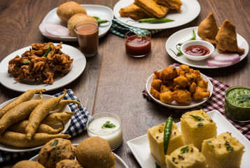 Indian Tea time snacks  in group includes Veg Samosa, Kachori/kachaudi, aloo bonda, khaman dhokla, bread, onion,chilli and moong pakora/pakoda/bhaji/bhajji/Bhajiya/bajji with sauces, selective focus