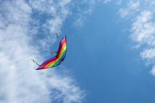 Multicolored kite on the background of the blue sky with clouds