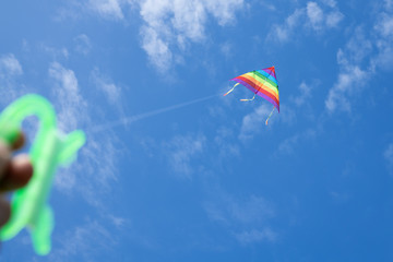 Multicolored kite on the background of the blue sky with clouds