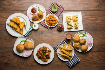 Indian Tea time snacks  in group includes Veg Samosa, Kachori/kachaudi, aloo bonda, khaman dhokla, bread, onion,chilli and moong pakora/pakoda/bhaji/bhajji/Bhajiya/bajji with sauces, selective focus
