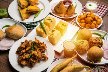 Indian Tea time snacks  in group includes Veg Samosa, Kachori/kachaudi, aloo bonda, khaman dhokla, bread, onion,chilli and moong pakora/pakoda/bhaji/bhajji/Bhajiya/bajji with sauces, selective focus