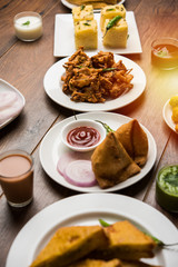 Indian Tea time snacks  in group includes Veg Samosa, Kachori/kachaudi, aloo bonda, khaman dhokla, bread, onion,chilli and moong pakora/pakoda/bhaji/bhajji/Bhajiya/bajji with sauces, selective focus