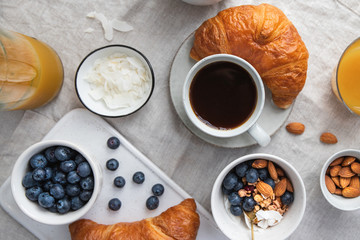 Top view of breakfast table with coffee, croissant, granola, nuts, berries and milk. Flat lay, healthy eating concept.