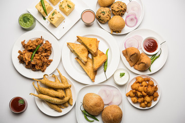 Indian Tea time snacks  in group includes Veg Samosa, Kachori/kachaudi, aloo bonda, khaman dhokla, bread, onion,chilli and moong pakora/pakoda/bhaji/bhajji/Bhajiya/bajji with sauces, selective focus
