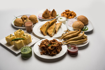 Indian Tea time snacks  in group includes Veg Samosa, Kachori/kachaudi, aloo bonda, khaman dhokla, bread, onion,chilli and moong pakora/pakoda/bhaji/bhajji/Bhajiya/bajji with sauces, selective focus