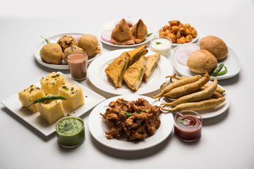Indian Tea time snacks  in group includes Veg Samosa, Kachori/kachaudi, aloo bonda, khaman dhokla, bread, onion,chilli and moong pakora/pakoda/bhaji/bhajji/Bhajiya/bajji with sauces, selective focus