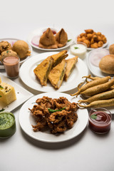 Indian Tea time snacks  in group includes Veg Samosa, Kachori/kachaudi, aloo bonda, khaman dhokla, bread, onion,chilli and moong pakora/pakoda/bhaji/bhajji/Bhajiya/bajji with sauces, selective focus