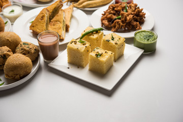 Indian Tea time snacks  in group includes Veg Samosa, Kachori/kachaudi, aloo bonda, khaman dhokla, bread, onion,chilli and moong pakora/pakoda/bhaji/bhajji/Bhajiya/bajji with sauces, selective focus