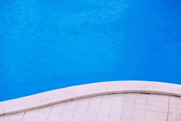 Summer storm, a fine rain falls on the blue water of a swimming pool in a hotel.