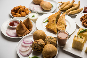 Indian Tea time snacks  in group includes Veg Samosa, Kachori/kachaudi, aloo bonda, khaman dhokla, bread, onion,chilli and moong pakora/pakoda/bhaji/bhajji/Bhajiya/bajji with sauces, selective focus