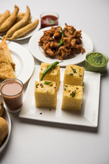 Indian Tea time snacks  in group includes Veg Samosa, Kachori/kachaudi, aloo bonda, khaman dhokla, bread, onion,chilli and moong pakora/pakoda/bhaji/bhajji/Bhajiya/bajji with sauces, selective focus