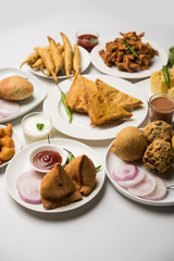 Indian Tea time snacks  in group includes Veg Samosa, Kachori/kachaudi, aloo bonda, khaman dhokla, bread, onion,chilli and moong pakora/pakoda/bhaji/bhajji/Bhajiya/bajji with sauces, selective focus