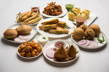 Indian Tea time snacks  in group includes Veg Samosa, Kachori/kachaudi, aloo bonda, khaman dhokla, bread, onion,chilli and moong pakora/pakoda/bhaji/bhajji/Bhajiya/bajji with sauces, selective focus