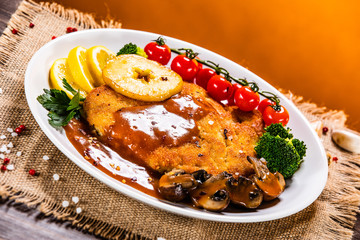 Fried pork chop with vegetables and mushrooms on wooden background