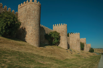 Fototapeta na wymiar Stone towers on the large city wall and green lawn at Avila