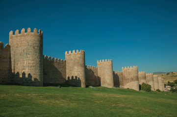 Fototapeta na wymiar Stone towers on the large city wall and green lawn at Avila