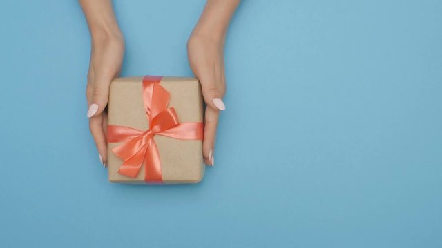 women's hands moving a box with a gift over a color studio background, girl giving a present, concept holidays, traditions and care