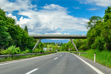 Autobahn or highway with a bridge in the mountains with clear marking surrounded by vibrant green...