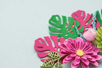 bright pink handmade paper flower; and pink and green monstera paper leaves against a blue background. copy space.