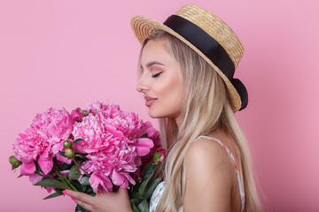 Beautiful young girl in straw hat with flowers peonies in hands on pink background