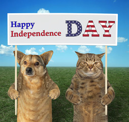 The dog and cat patriot holds a sign (Happy Independence Day) together on the meadow.