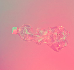 Minimalism pollution ecology concept. Crumpled plastic bottle in neon red blue light