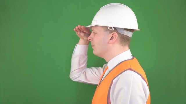 Male chief foreman in a protective helmet and signal vest looks into the distance on a construction site, green background, hromakey