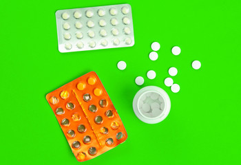Blisters and a bottle of pills on green background.