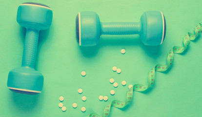 Sport weight loss concept. Dumbbells, ruler, pills on a blue background. Minimalism. Top view