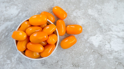 small bowl overflowing with bright orange grape tomatoes on a gray marble counter viewed from above with copy space