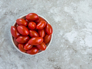 small bowl filled with bright red grape tomatoes on a gray marble counter viewed from above with copy space