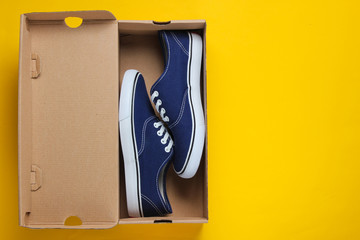 New trendy sneakers in cardboard box on yellow background. Top view