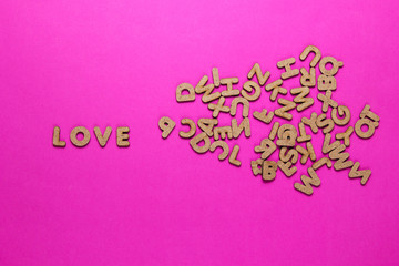 The word love among wooden letters on pink background. Top view