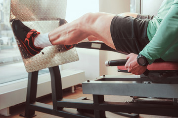 Strong active man is doing legs exercises on training apparatus in gym