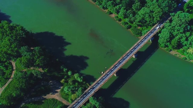 4K aerial top down view of cars missing one another, driving along long bridge, over calm green water river. 4K.