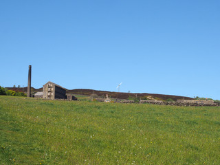 Obraz premium a bright green grass meadow covered in on a hillside with the old mill chimney and stone house houses at old town near hebden bridge west yorkshire