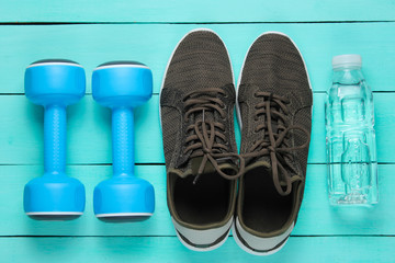 Minimalistic fitness concept. Dumbbells, sneakers, bottle of water on blue wooden background. Top view