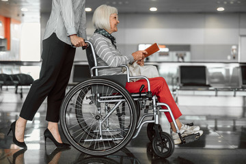 Female worker moving elderly woman on disabled carriage boarding