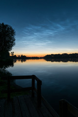Tranquil scene after sunset near the calm water of a lake with shining night clouds (NLC or noctilucent clouds) in the sky