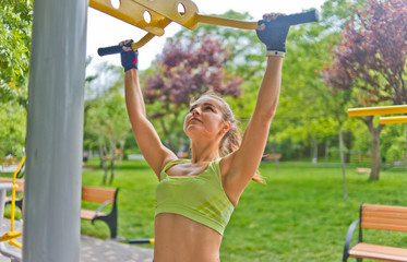 Obraz premium Young woman pulls herself up on a horizontal bar in the park