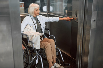 Mature woman in glasses on disabled carriage using elevator © Yakobchuk Olena