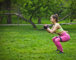 Sporty woman doing squats with fitness gum expander in the park outdoors