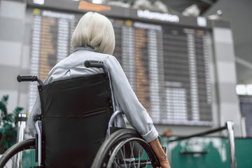 Elderly woman on wheelchair looking on flight schedule